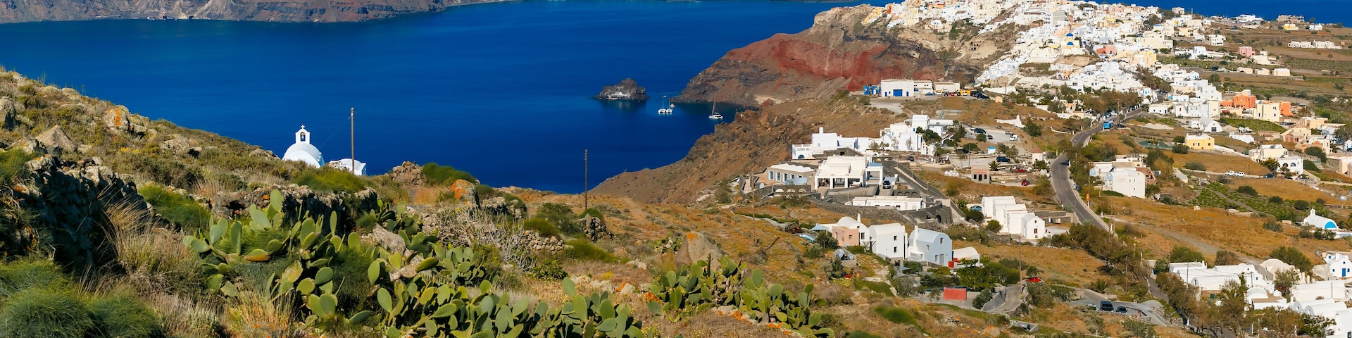 Aerial panoramic view of Oia or Ia and Finikia on the island Santorini, white houses, windmills and church with blue domes, Greece