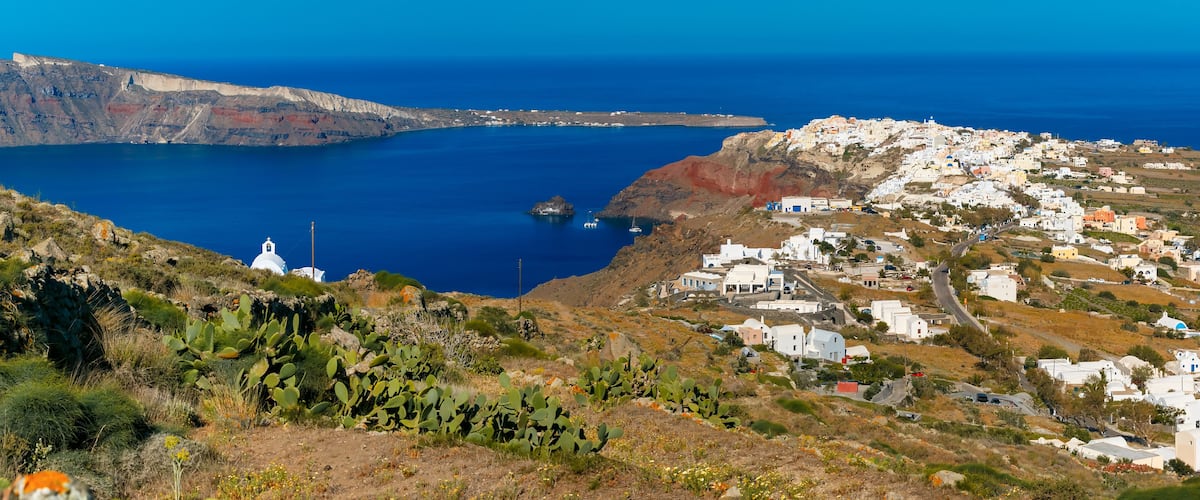 A coastal town with white buildings, a clear blue sea, and a rocky landscape with cacti.