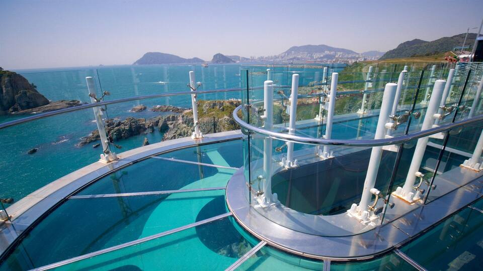 A glass-bottomed infinity pool overlooking a coastal landscape with clear blue waters and distant mountains.