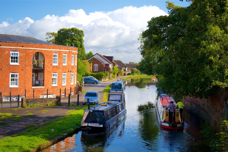 A canal with boats, a brick building, and a car parked on the side.
