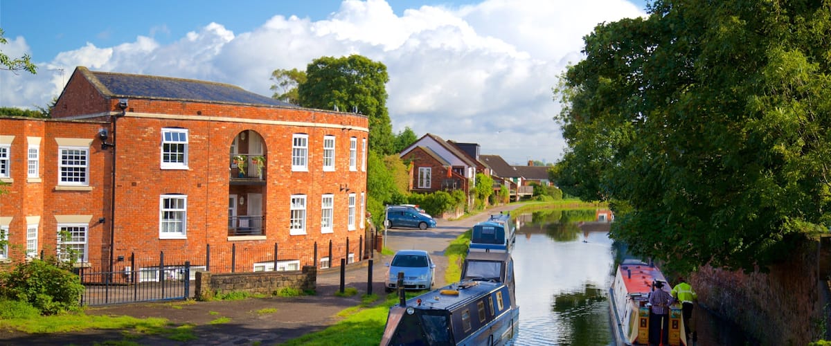 A canal with boats, a brick building, and a car parked on the side.