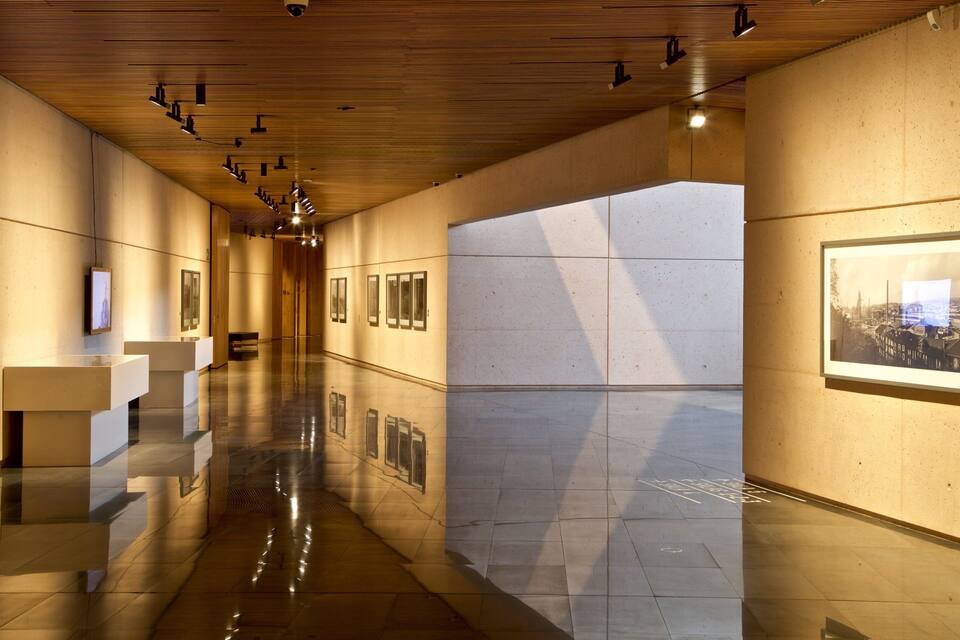 Una galleria d'arte moderna con pavimento lucido, soffitto in legno e opere incorniciate alle pareti.