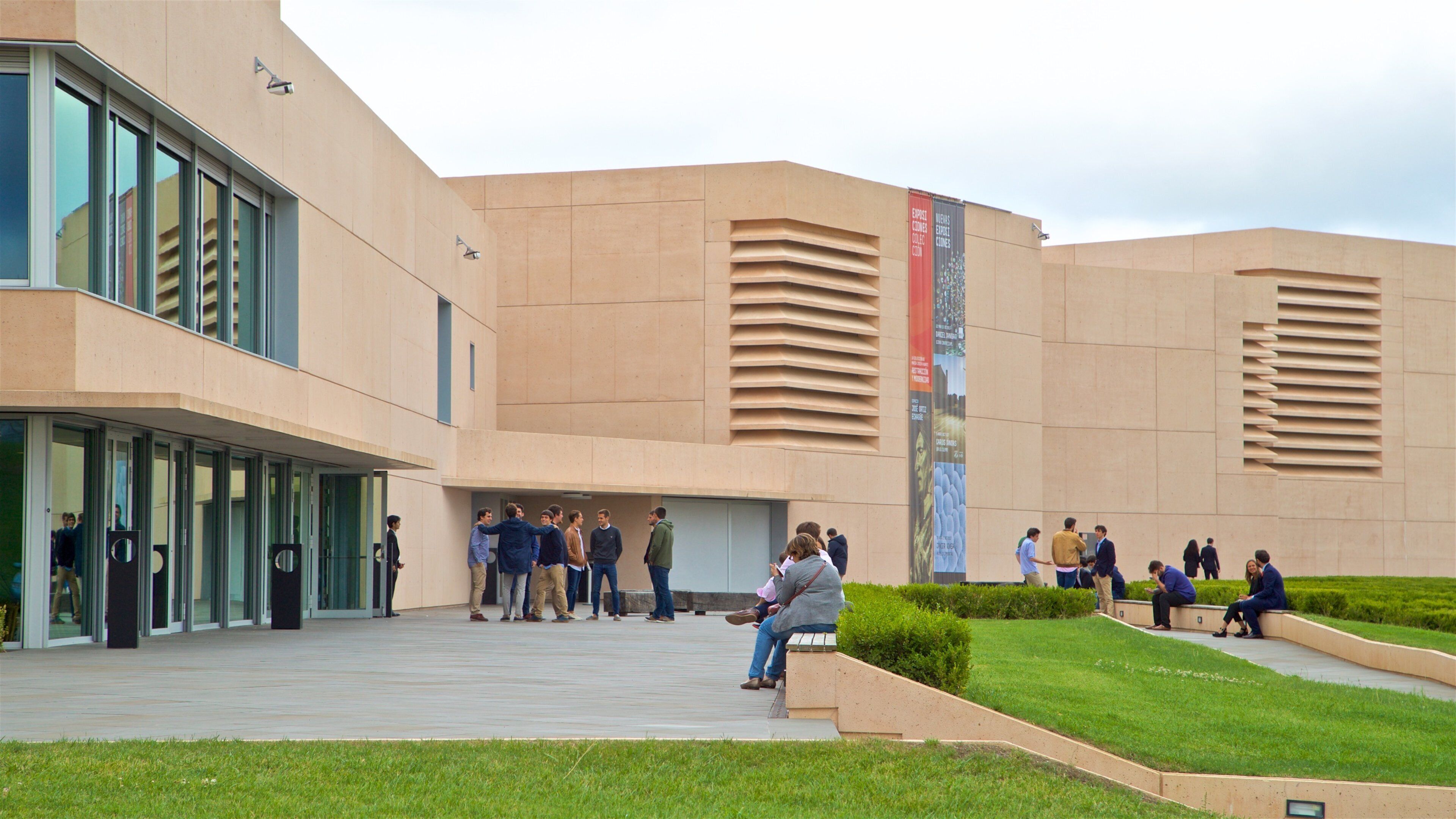 Un bâtiment moderne doté d’une grande entrée en verre et où se trouve un groupe de personnes rassemblées à l’extérieur.