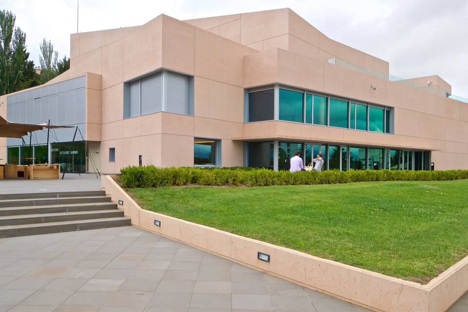 A modern building with a flat roof, large windows, and a paved courtyard with steps leading to the entrance.