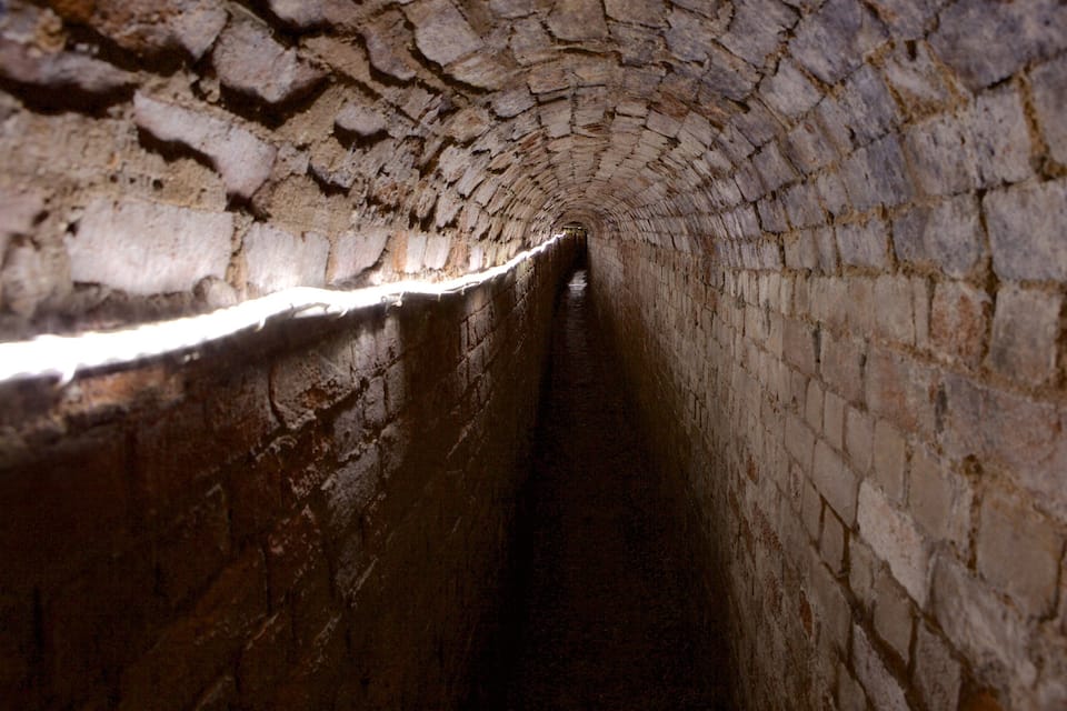 Un túnel de piedra estrecho y arqueado, con paredes rugosas e irregulares.