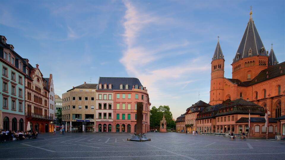 A historic square with a prominent church tower, colorful buildings, and a fountain.