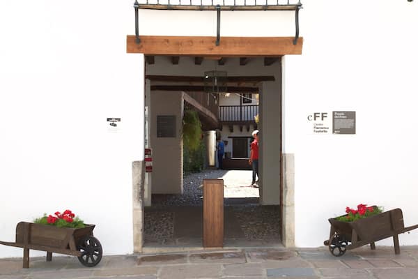 Uma entrada rústica com vigas de madeira, um portão de metal e jardineiras com flores sobre rodas.