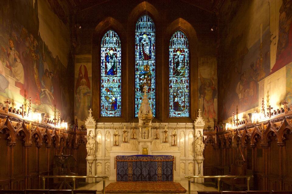 A church interior with stained glass windows, altar, and ornate woodwork.