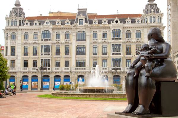 Eine Statue einer Frau, die ein Kind hält, vor einem großen, verzierten Gebäude mit einem Brunnen in der Mitte.