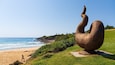 A sculpture on a grassy hill overlooking a beach with waves.
