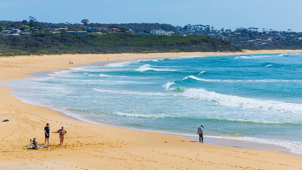A sandy beach with waves, footprints, and a few people.