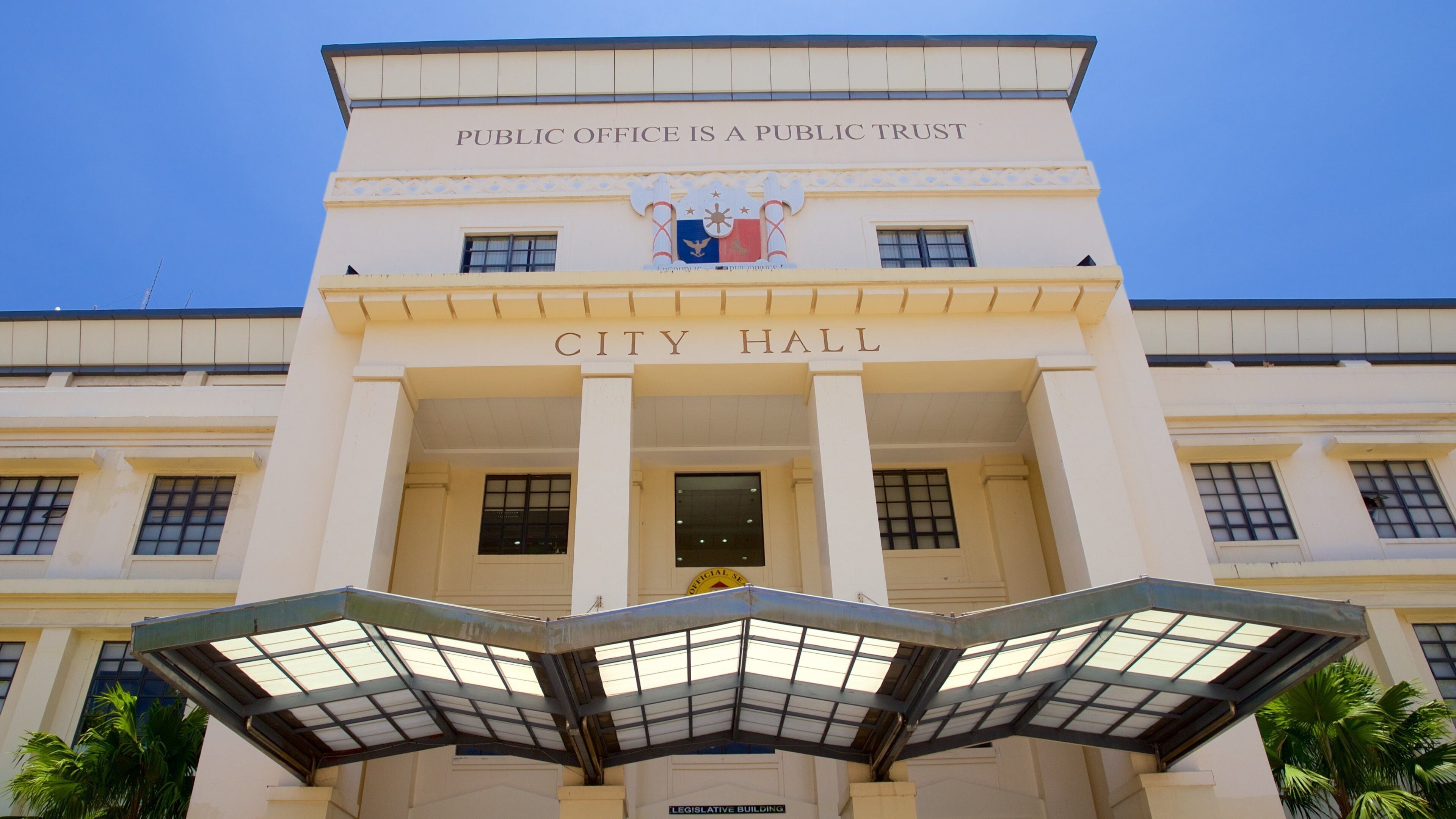A city hall with a sign stating "Public Office is a Public Trust" and "City Hall" above the entrance.