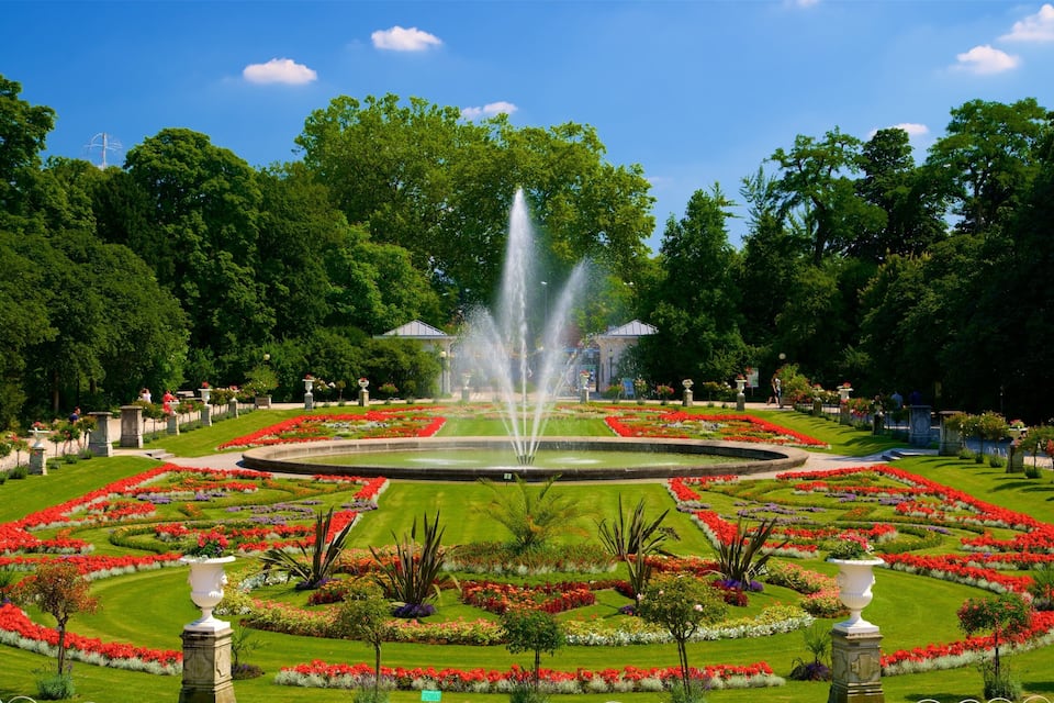 A formal garden with a central fountain, manicured lawns, and flower beds.