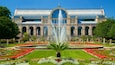 A large building with a fountain in front, surrounded by a well-maintained garden with various flowers and plants.