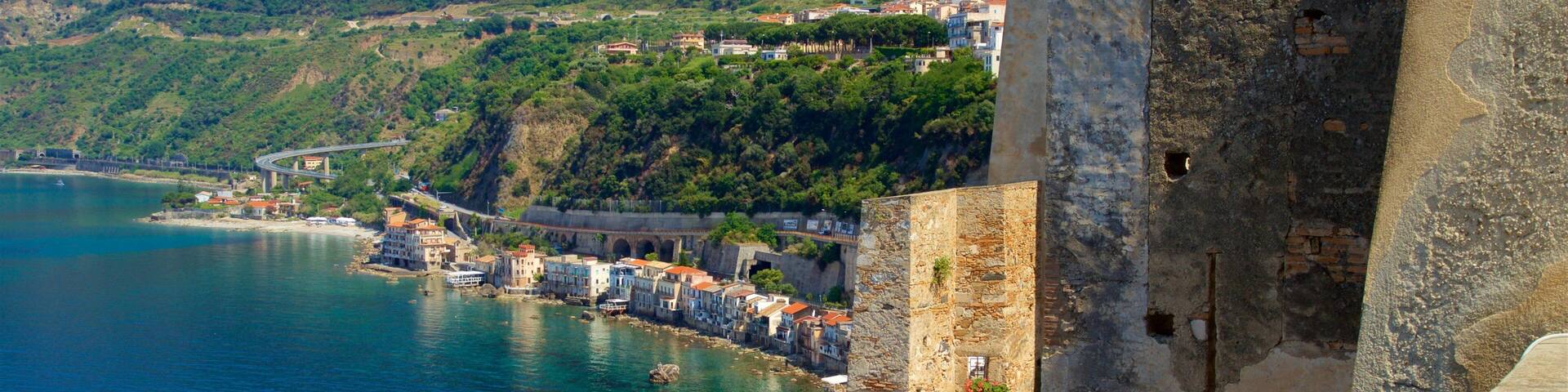 A coastal town with a historic fortification, a bridge, and lush green hills in the background.
