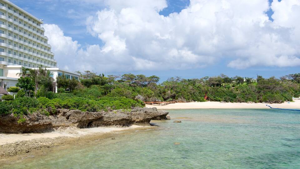 A beach with clear turquoise water, white sand, and lush greenery.
