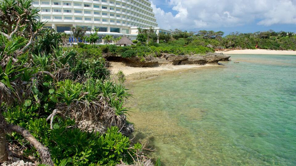 A beach with clear turquoise water, lush greenery, and a large resort building in the background.