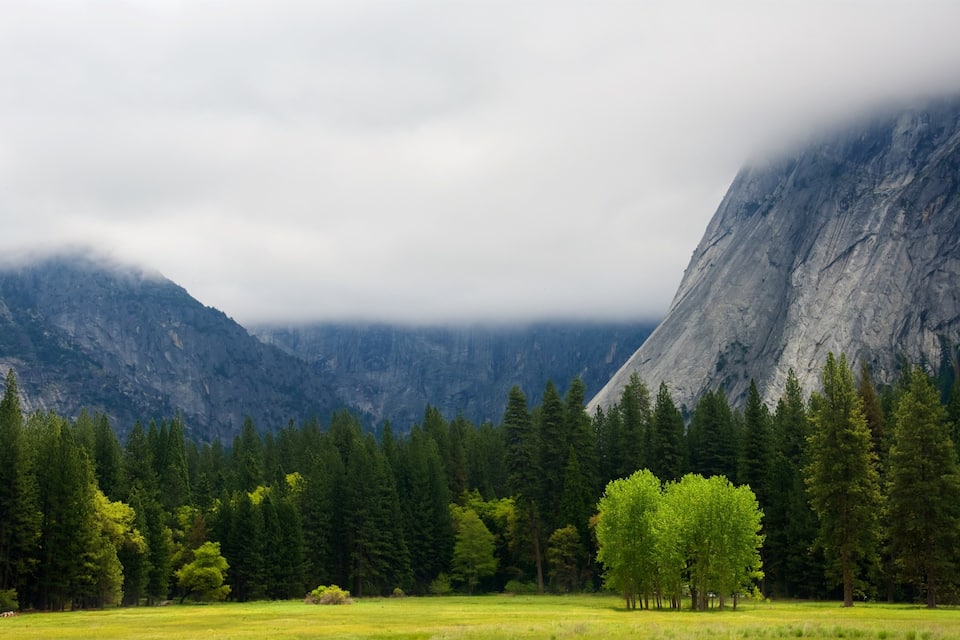 A mountainous landscape with a prominent rock face, dense forest, and a clear sky.