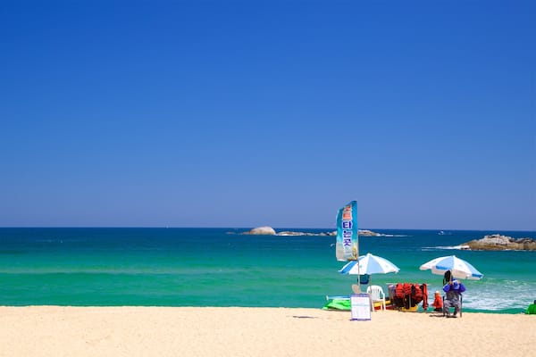 A beach with clear turquoise water, a rocky outcrop, and a flag.