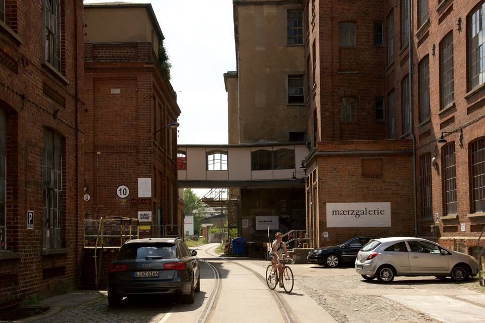 A narrow street with brick buildings, parked cars, and a cyclist.