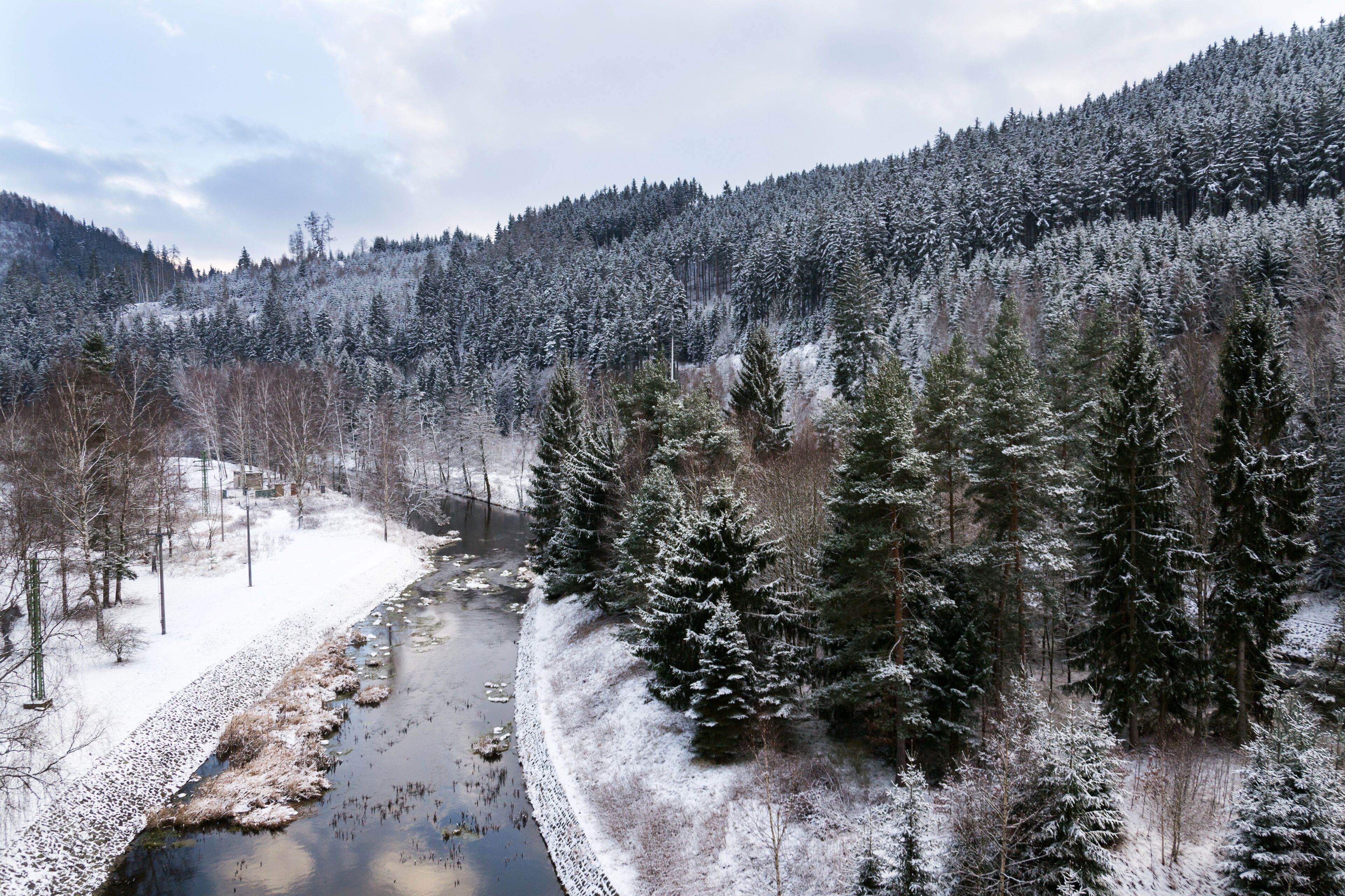 A snow-covered river valley with dense coniferous forests and a mountainous backdrop.