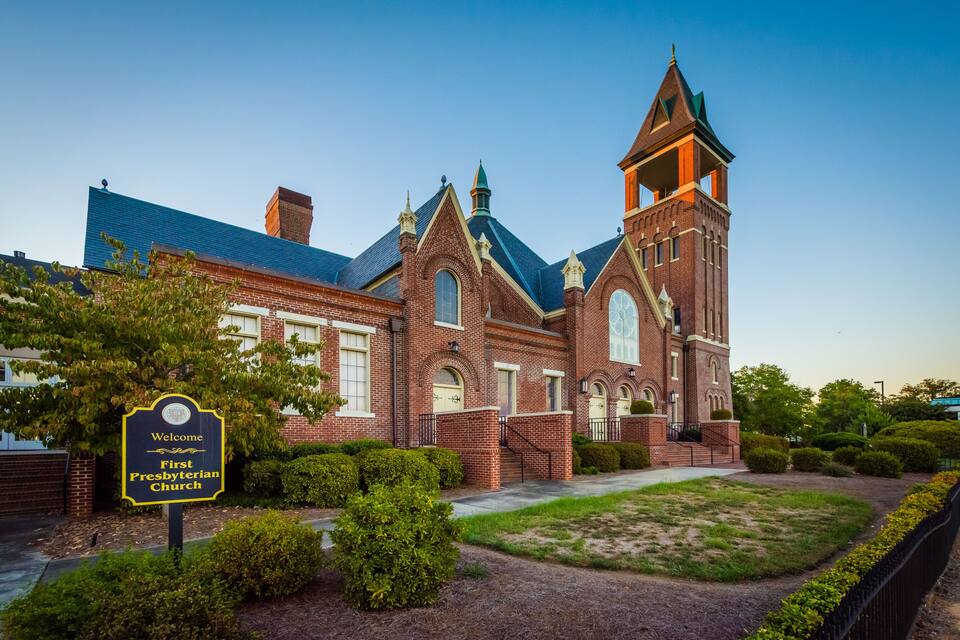 A brick church with a steeple and a sign reading "Welcome First Presbyterian Church."