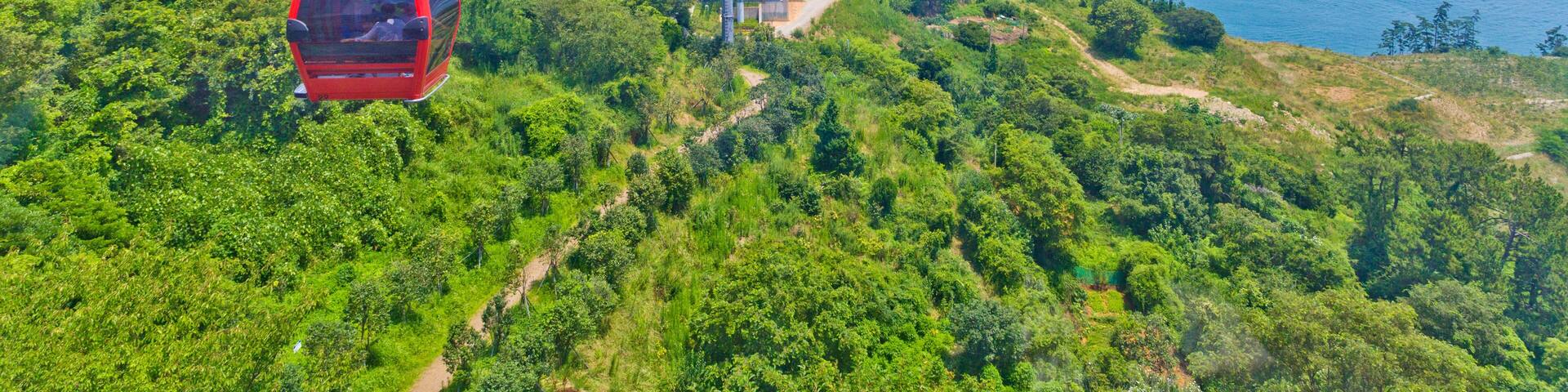 Un sistema de teleférico, exuberante vegetación y un paisaje costero con montañas al fondo.