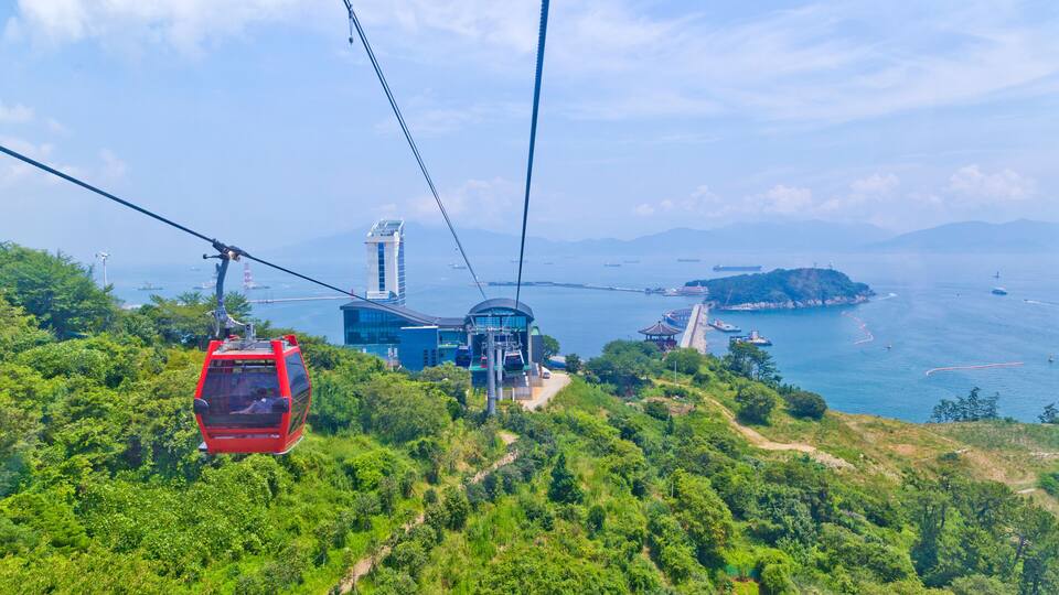 A cable car system, lush greenery, and a coastal landscape with mountains in the background.