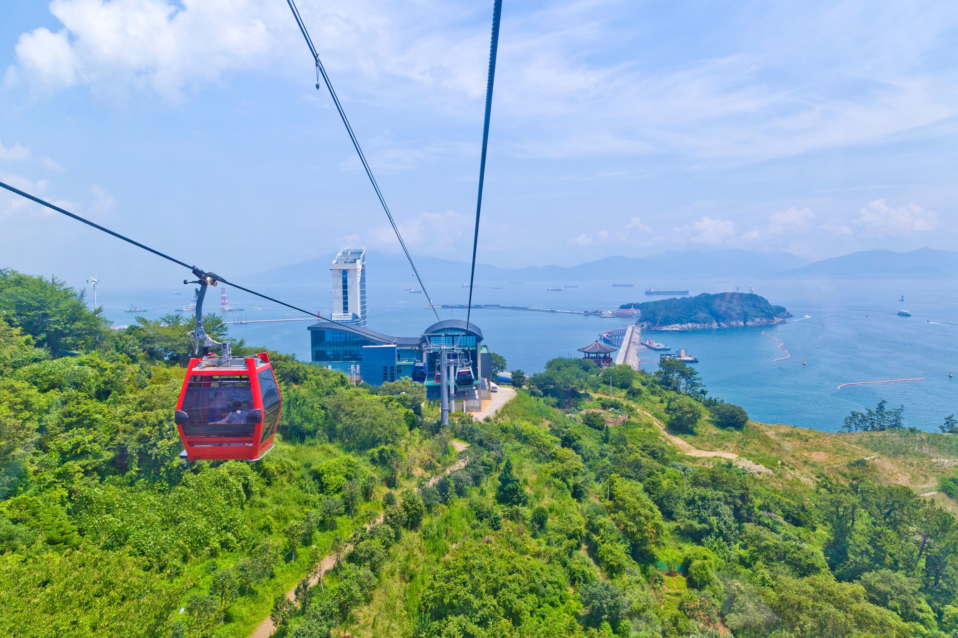 A cable car system, lush greenery, and a coastal landscape with mountains in the background.