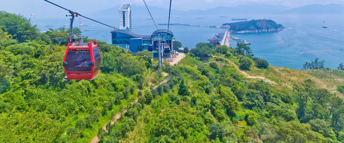 A cable car system, lush greenery, and a coastal landscape with mountains in the background.