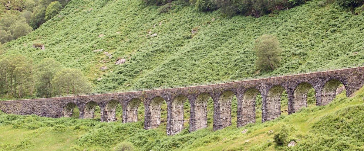 A stone viaduct with multiple arches spanning a lush green hillside.