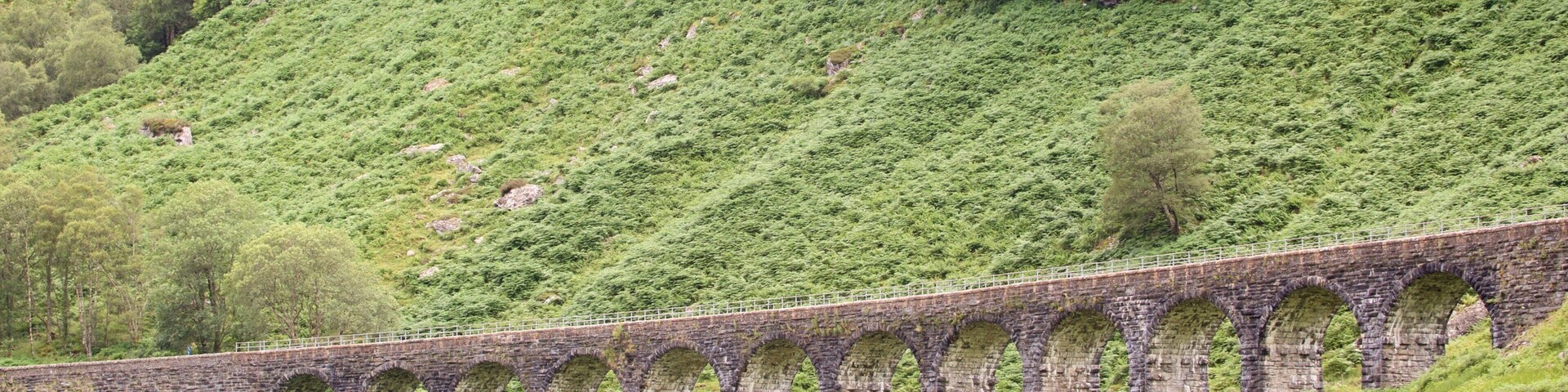 A stone viaduct with multiple arches spanning a lush green hillside.