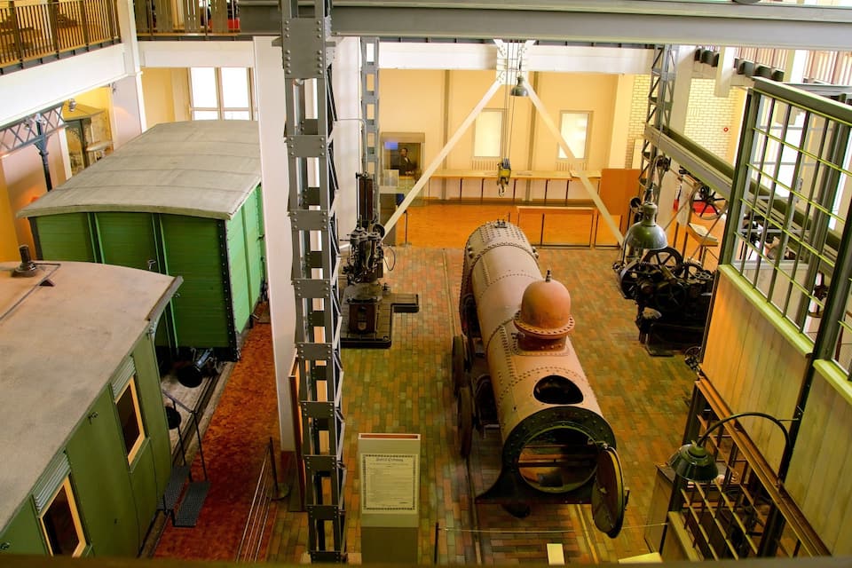 En stor, cylindrisk industrimotor med ett kupolformat toppstycke, placerad i en rymlig byggnad med flera våningar, utrustad med metallräcken och ett tegelfärgat golv.