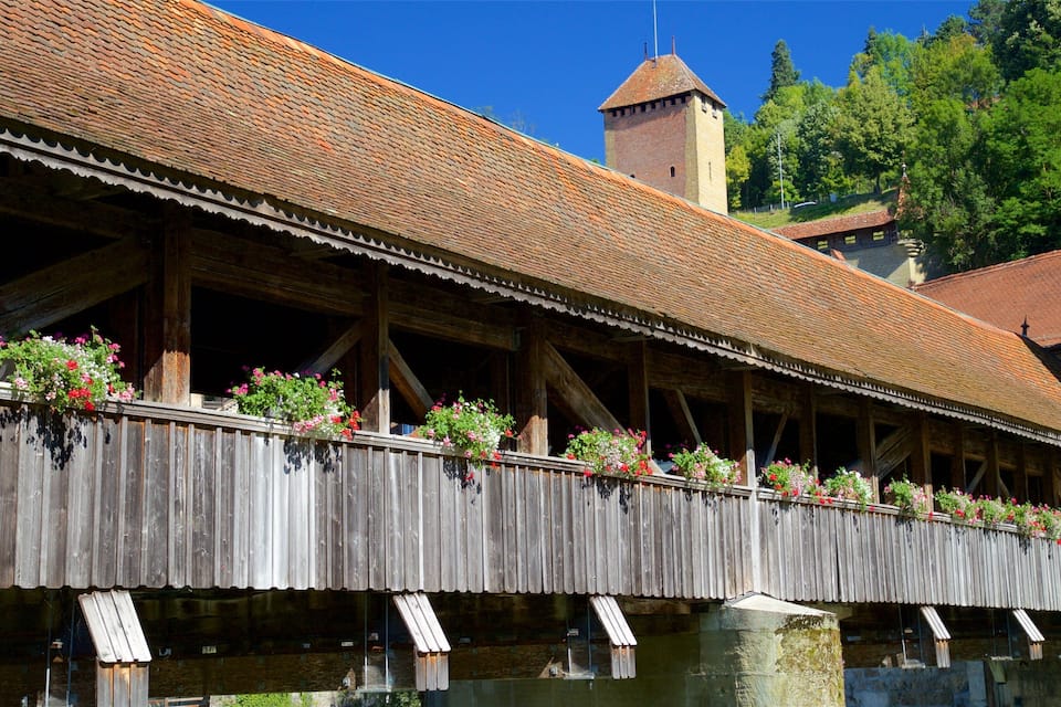 Un puente cubierto de madera con jardineras de flores y una torre al fondo.