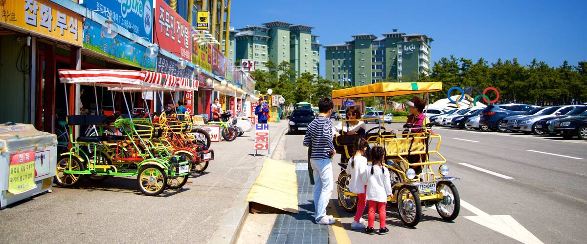 A street with colorful shops, a green bike rental, and a yellow tricycle.