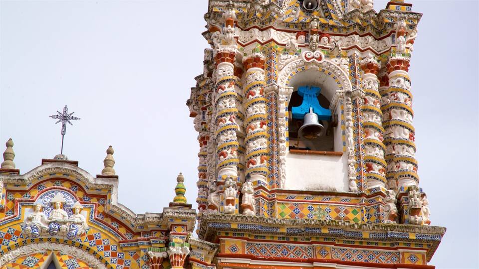 A colorful bell tower with intricate tile work and a cross on top.