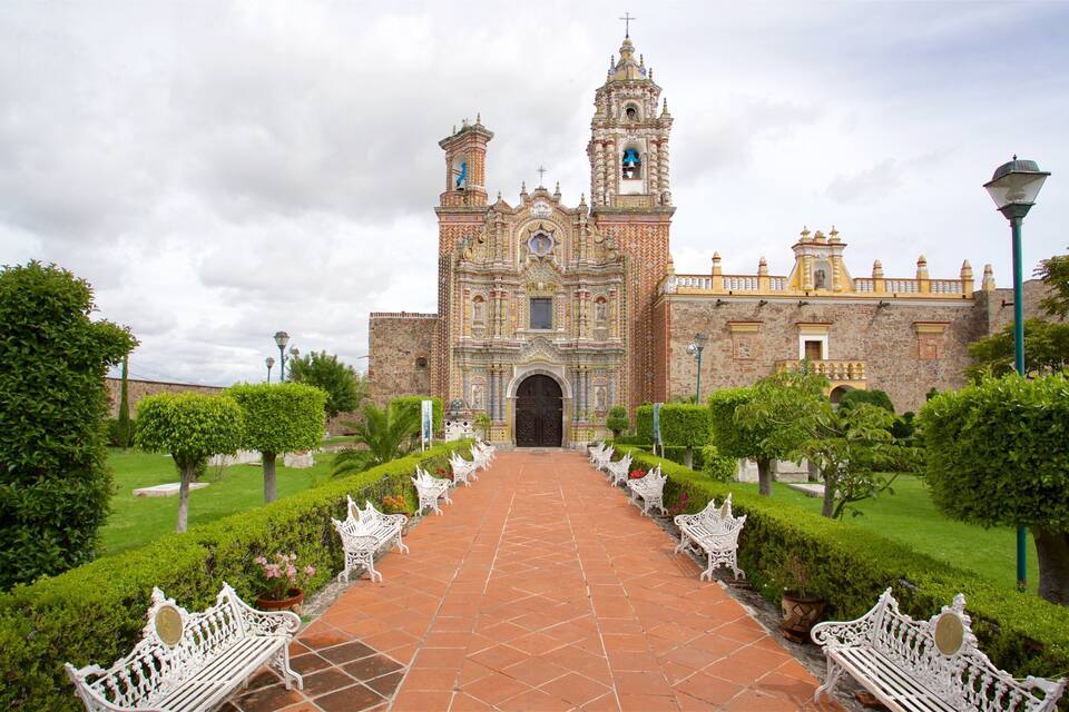 A historic church with intricate architecture, a central bell tower, and a symmetrical garden with benches.