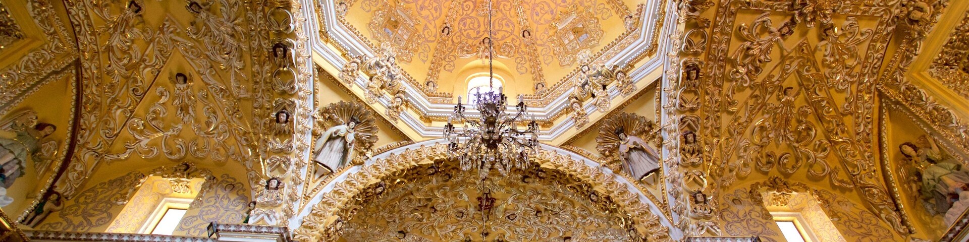 Un techo ornamentado con detalles en oro intrincados y un candelabro central.