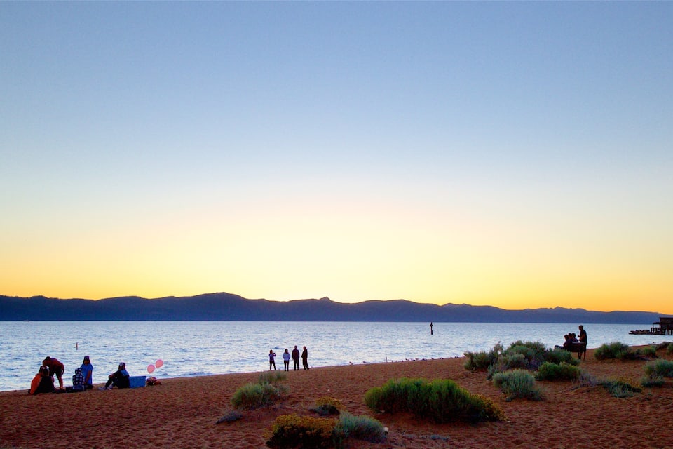 Una platja amb gent, un moll i muntanyes al fons.