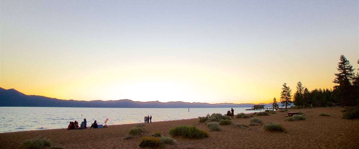 A beach at sunset with people relaxing and a pier in the background.