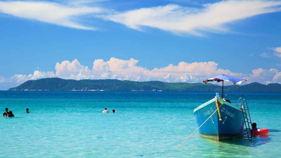 A clear blue sea with a boat and people swimming.