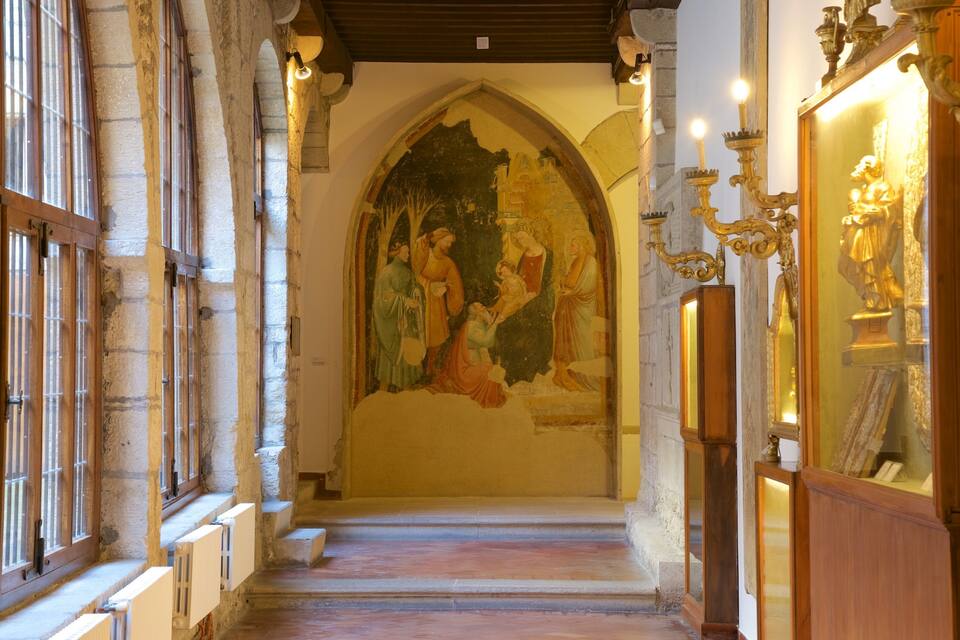 Ein Kircheninneres mit einer mittelalterlichen Wandmalerei, Bogenfenstern und einem hölzernen Altar.