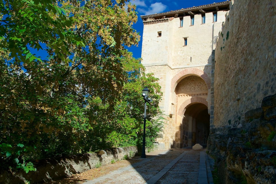 Un edificio de piedra con una entrada arqueada, rodeado de árboles y un camino adoquinado.