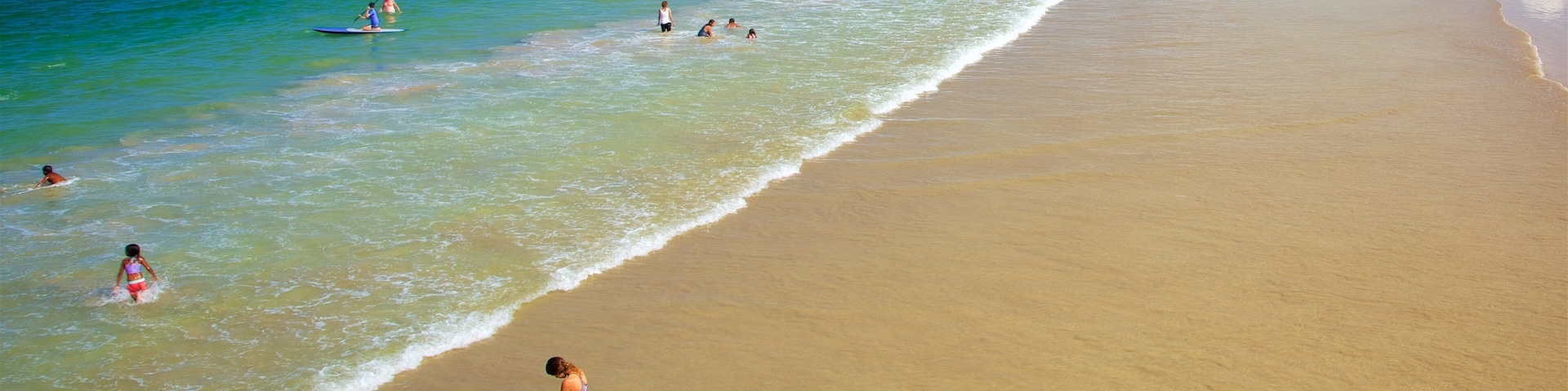 A beach with clear turquoise water, a sandy shore, and a few people in the water.