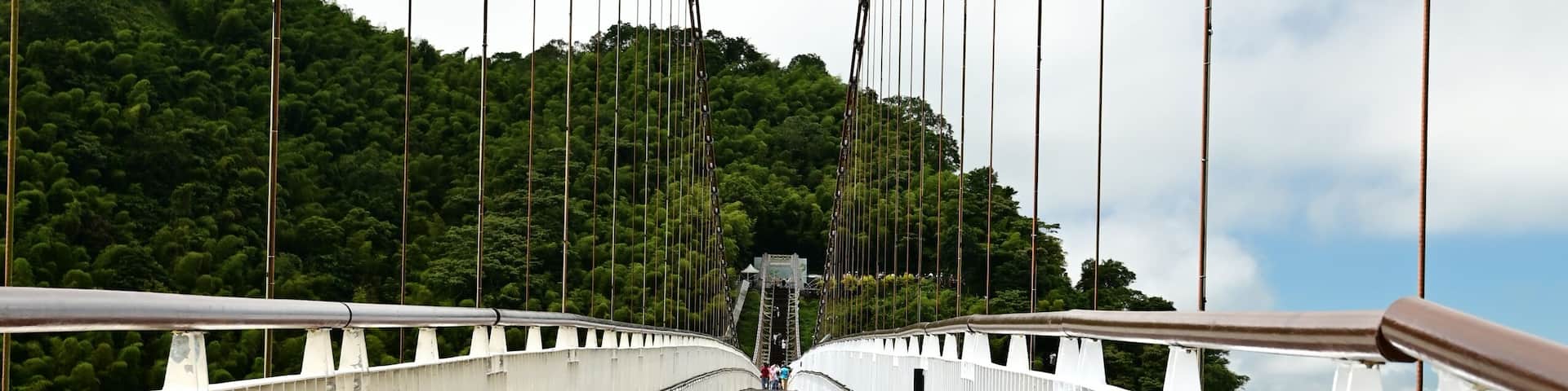 A wooden pedestrian bridge with white railings and cables, leading to a distant structure.