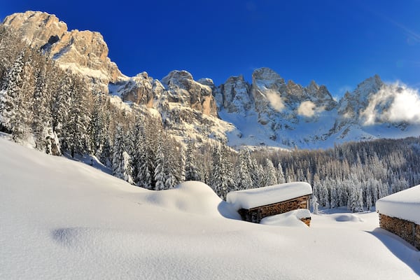 Un paysage montagneux enneigé, avec des chalets en bois et un ciel bleu dégagé.