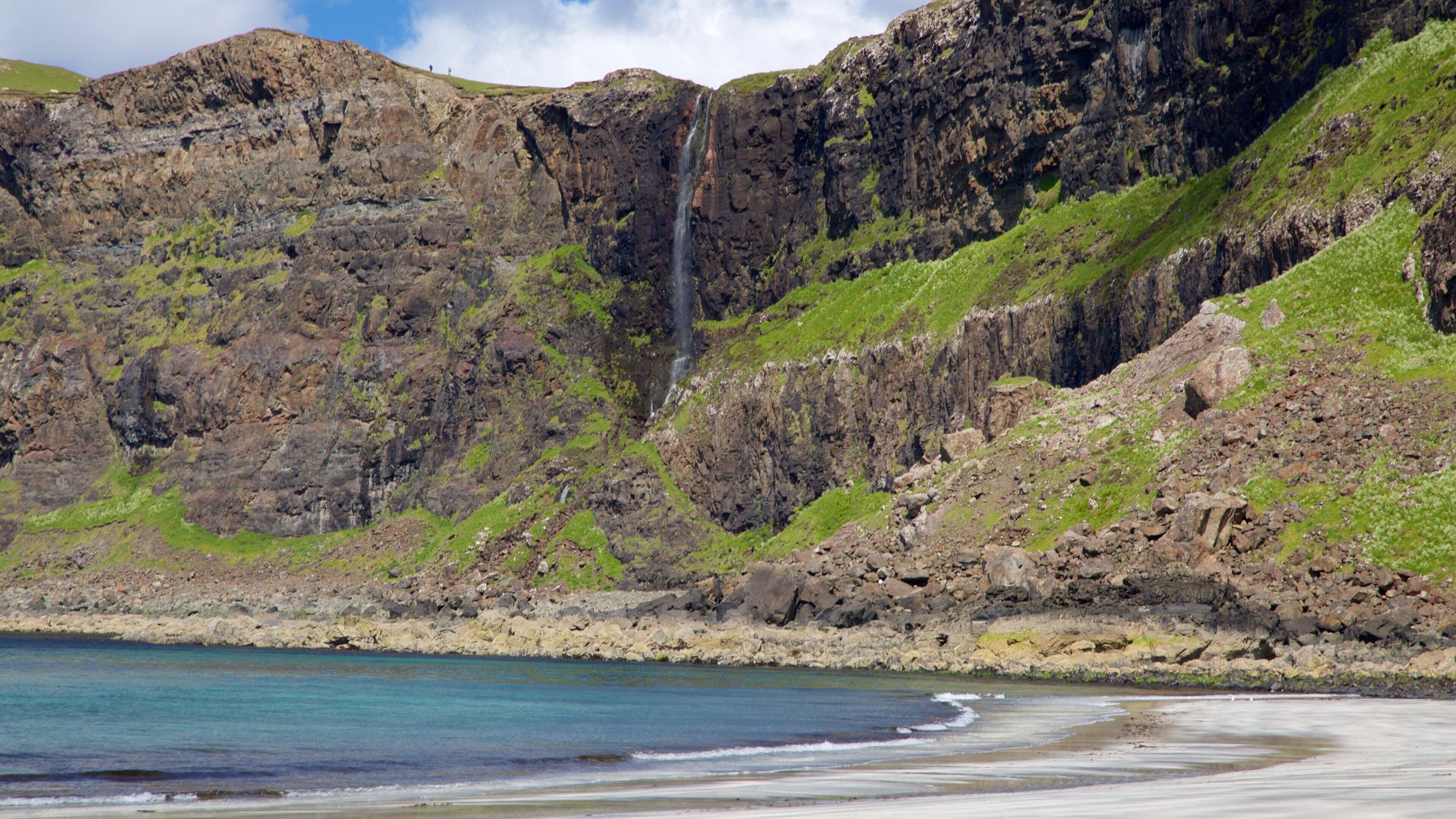 Un paysage côtier avec une cascade, des falaises rocheuses et une plage.