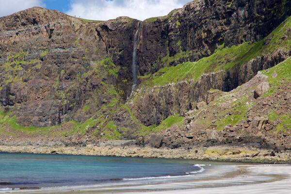 A coastal landscape with a waterfall, rocky cliffs, and a beach.