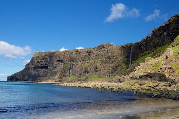 Eine Küstenlandschaft mit einer felsigen Klippe, einem Wasserfall und einem klaren, blauen Meer.