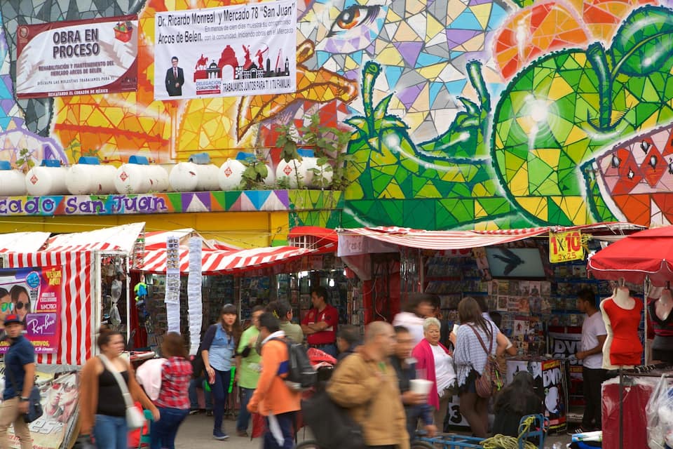 Um mercado de rua vibrante com murais coloridos e diversos pontos de venda oferecendo óculos de sol e outros produtos.